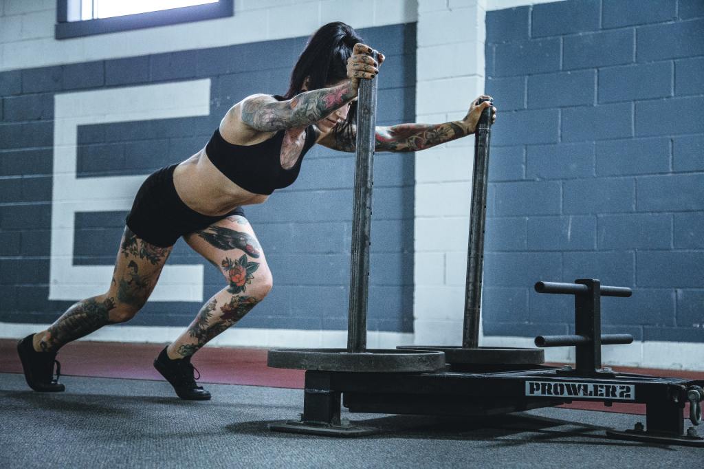Tattooed woman doing sled pull at the gym