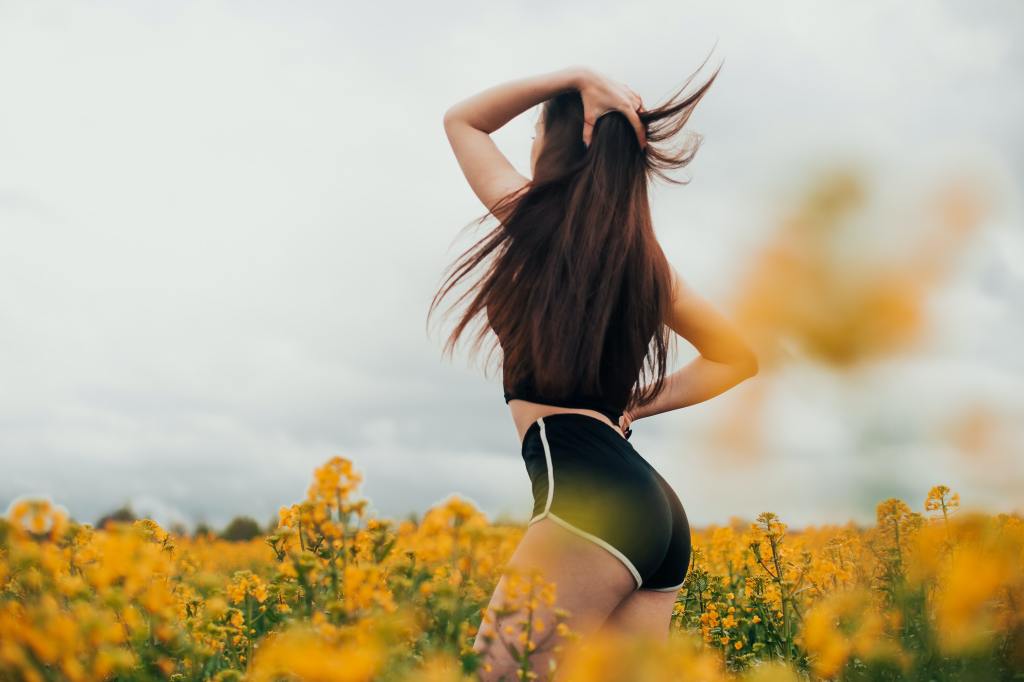 Women in shorts with long hair in a field of yellow flowers 
 
