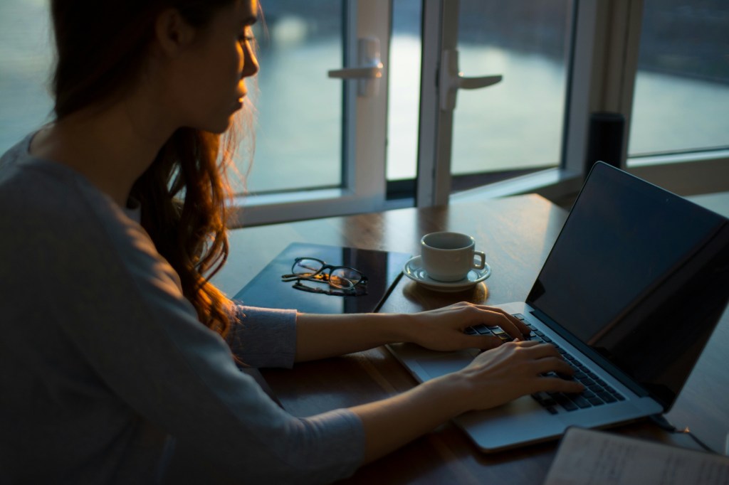 Woman on laptop working with cup of espresso next to her