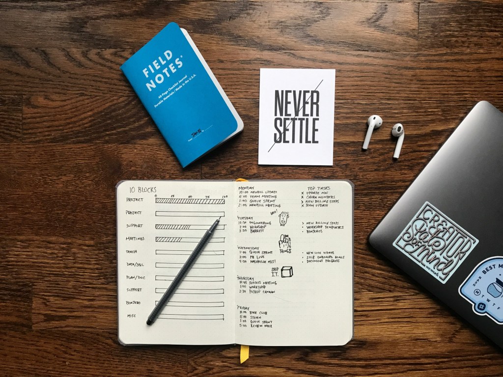 Organizer, notepad, earphones, laptop and sign that says “never settle”
