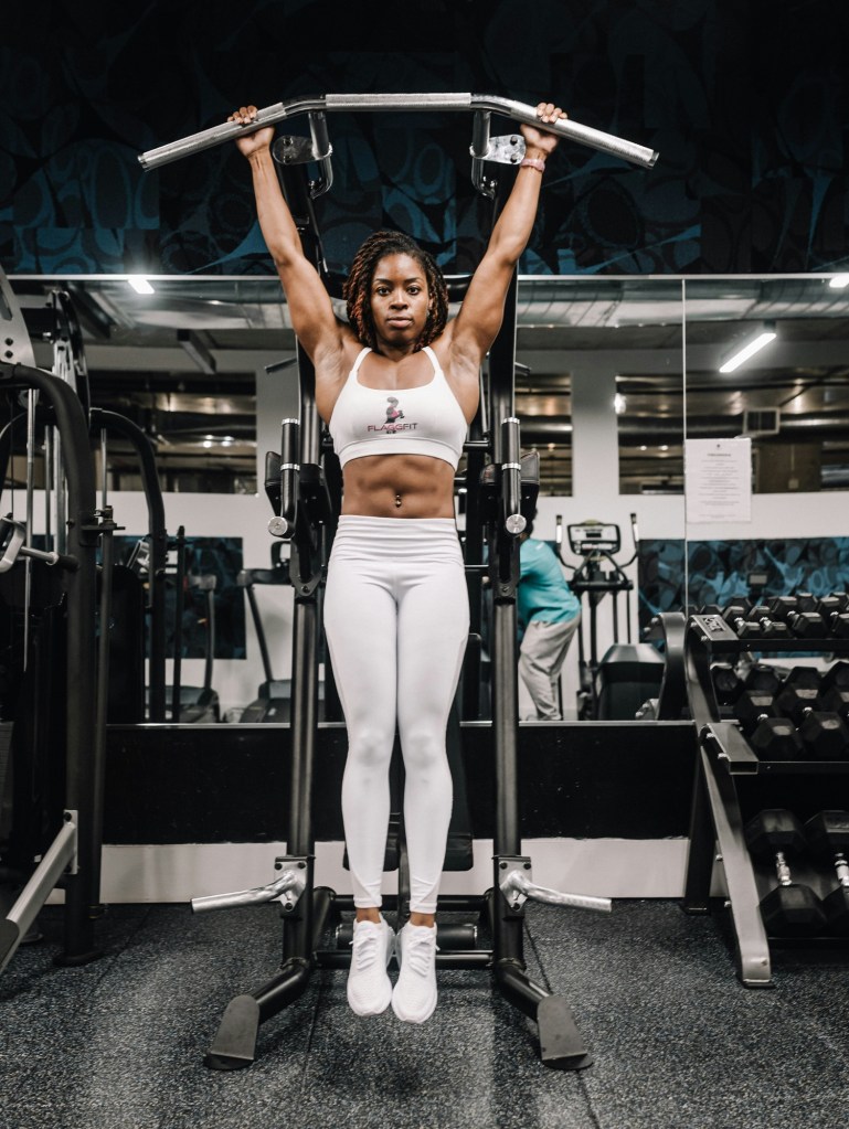 Woman hanging off of pull up bar with six pack abs 
